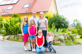 Eltern mit vier jüngeren Kindern vor Haus, möglicherweise Eigenheim